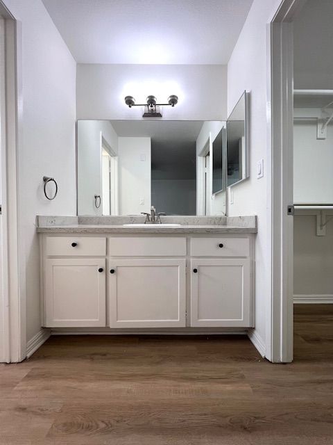 A bathroom with white cabinets , a sink and a mirror.