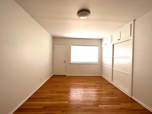 An empty room with hardwood floors , white walls and a window.