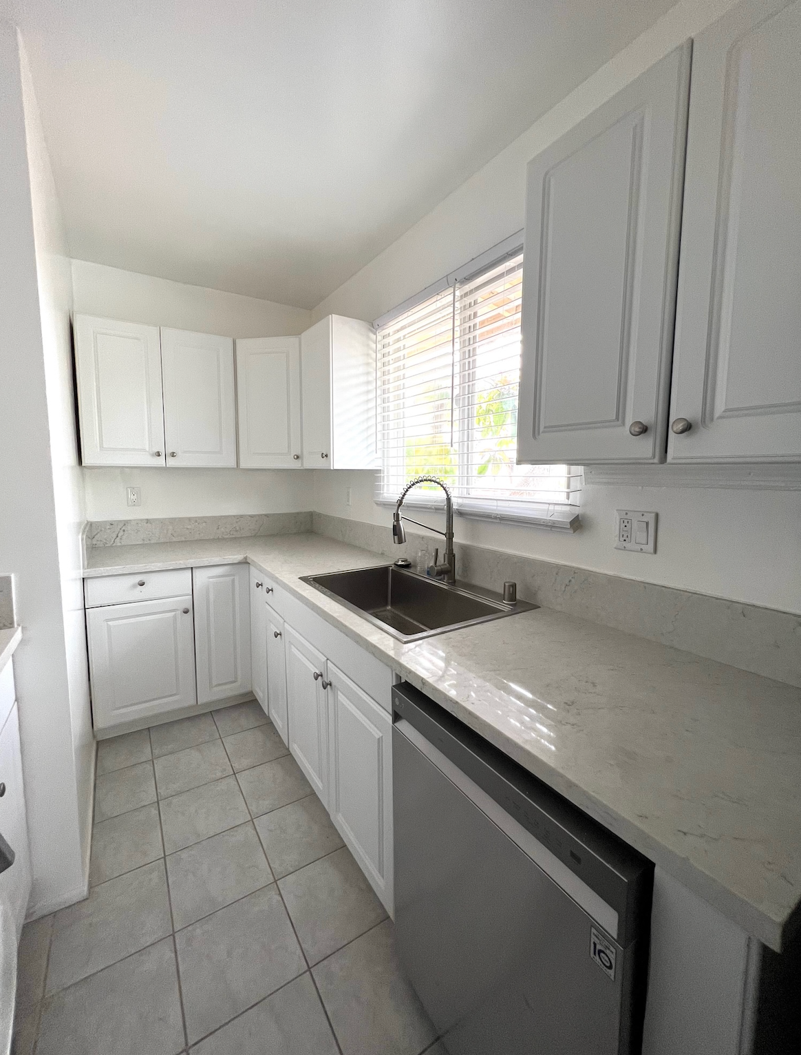 A kitchen with white cabinets , a sink , a dishwasher and a window.