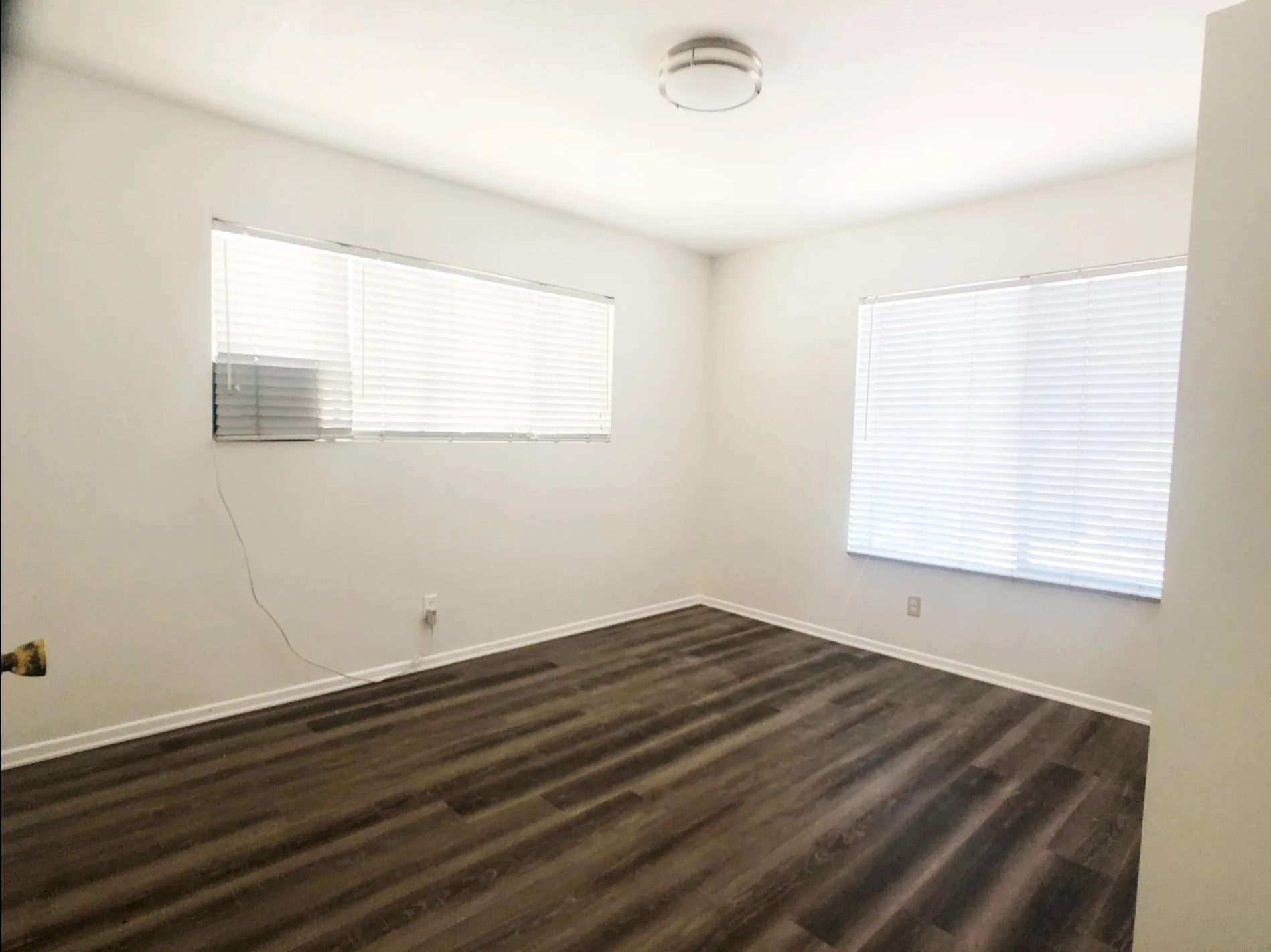 An empty bedroom with hardwood floors and two windows.