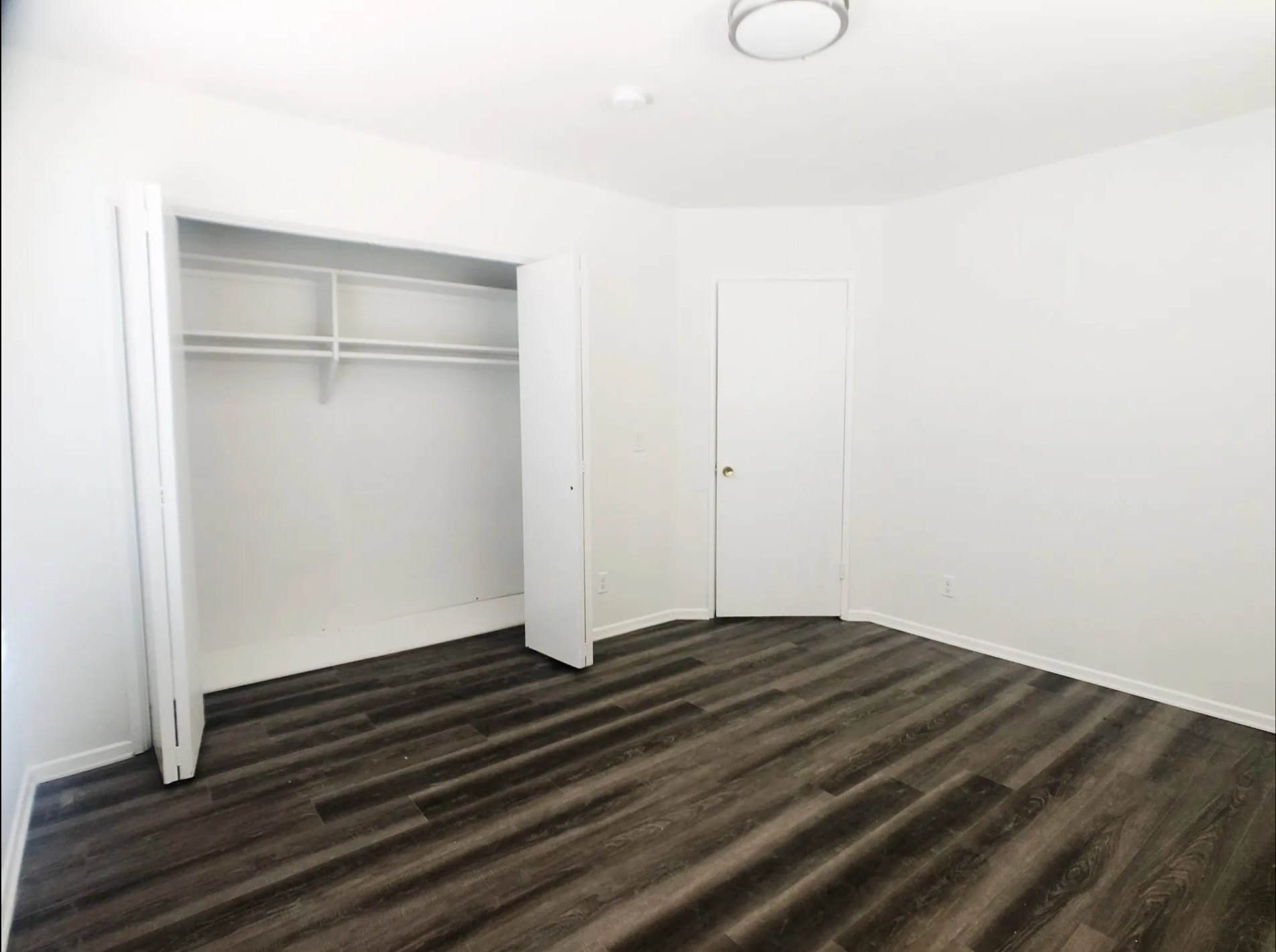 An empty bedroom with hardwood floors and a closet.