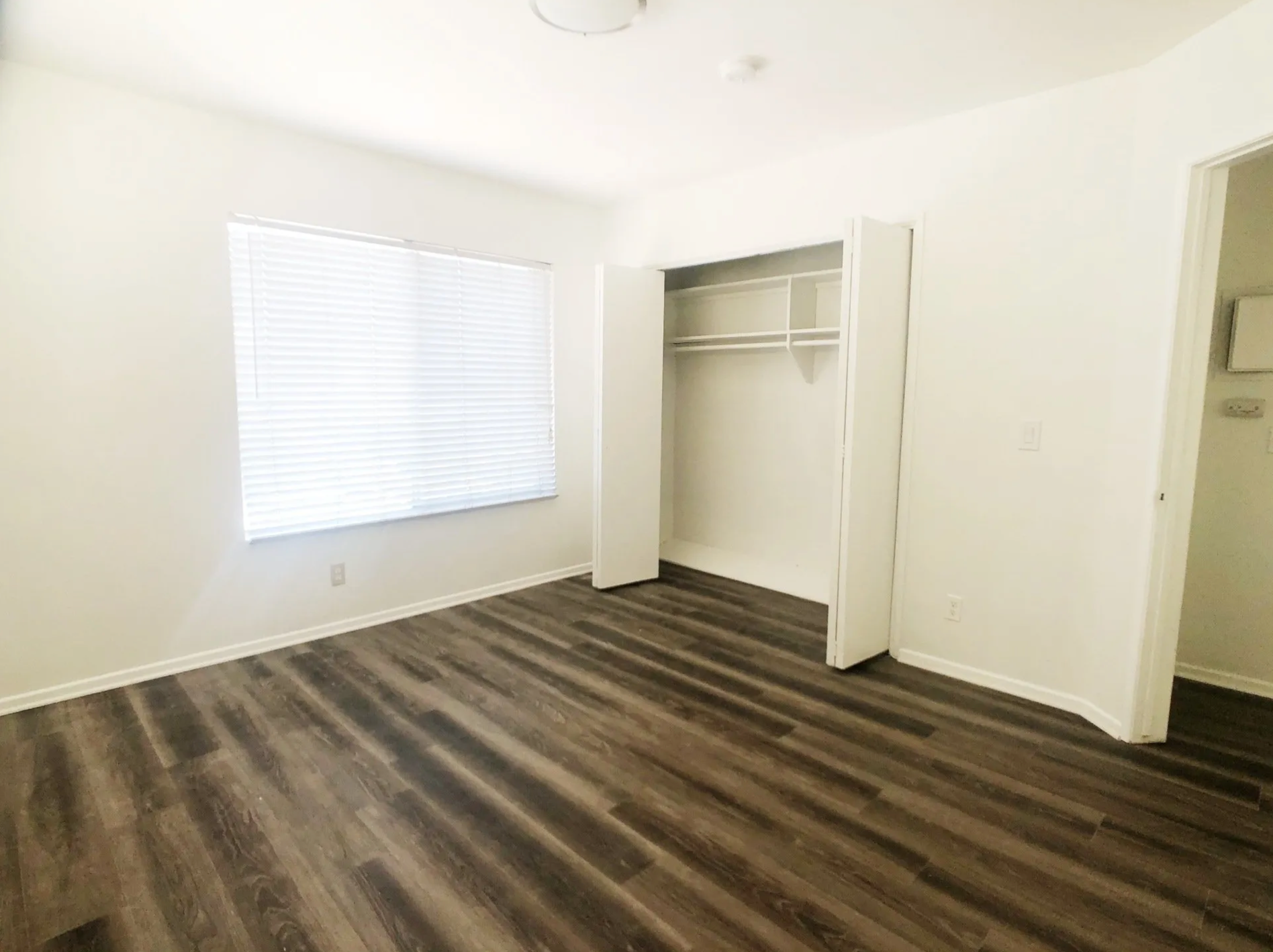 An empty bedroom with hardwood floors and a closet.