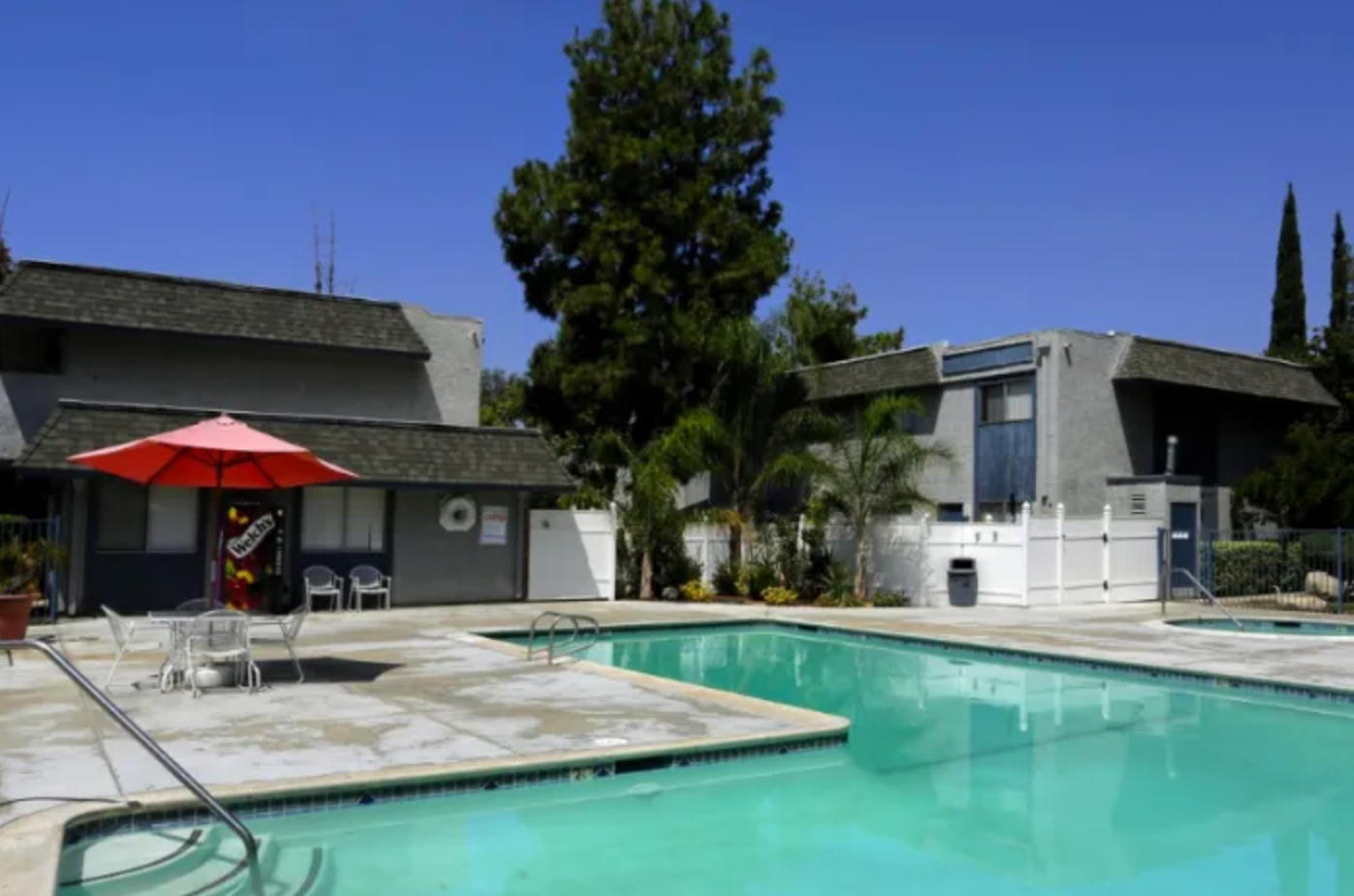 A large swimming pool with a red umbrella in front of a building