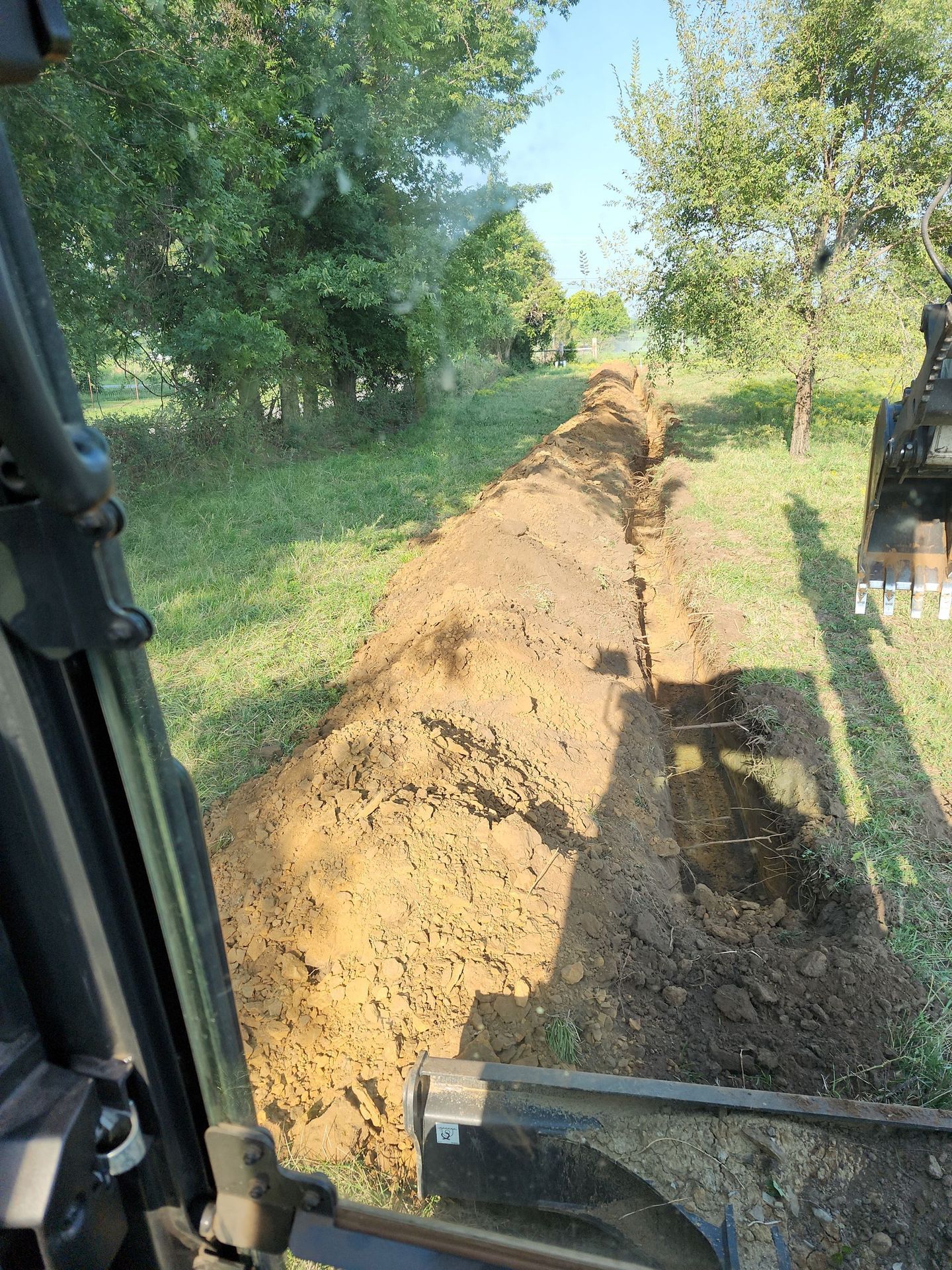 A trench dug through grassy land by an excavator; viewed from the cab.