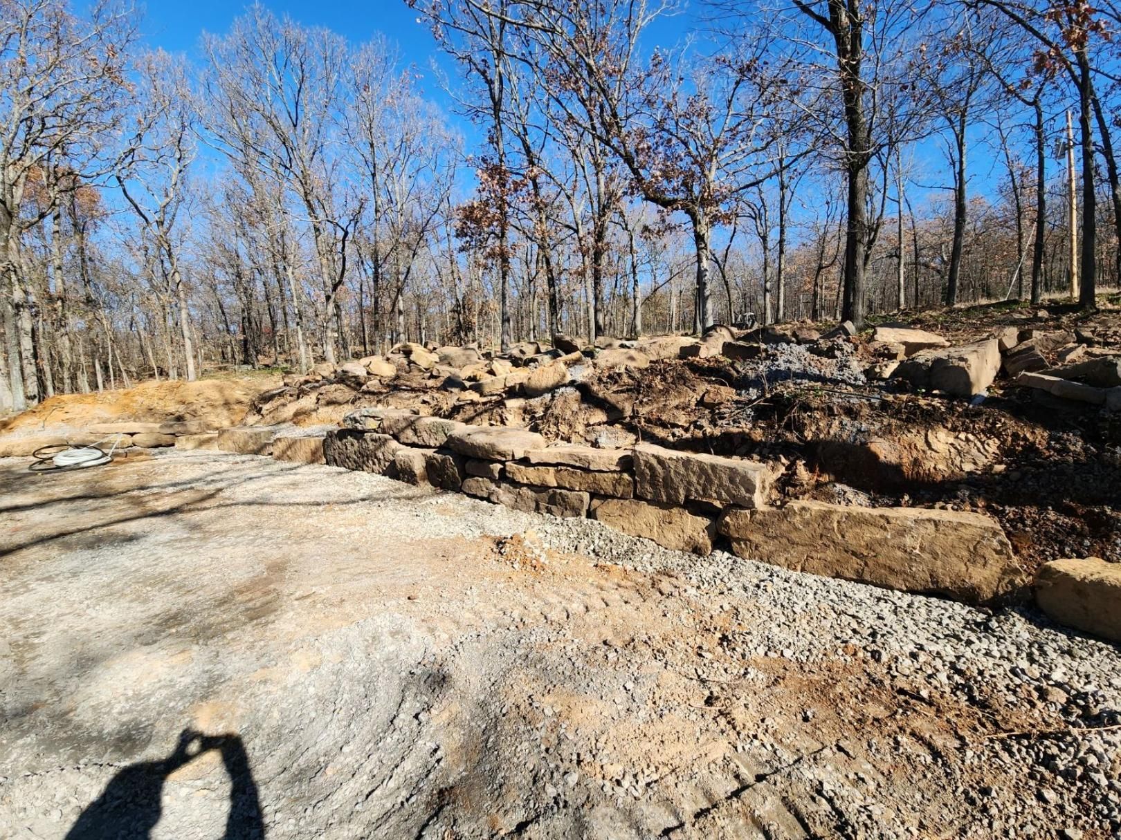A gravel driveway with a low stone retaining wall, set among bare trees under a bright blue sky.