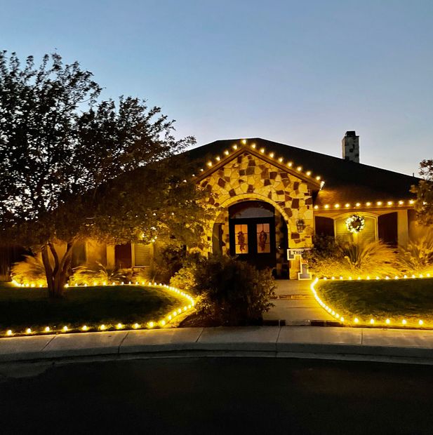 Stone house at dusk outlined with warm string lights along the roof and garden path.