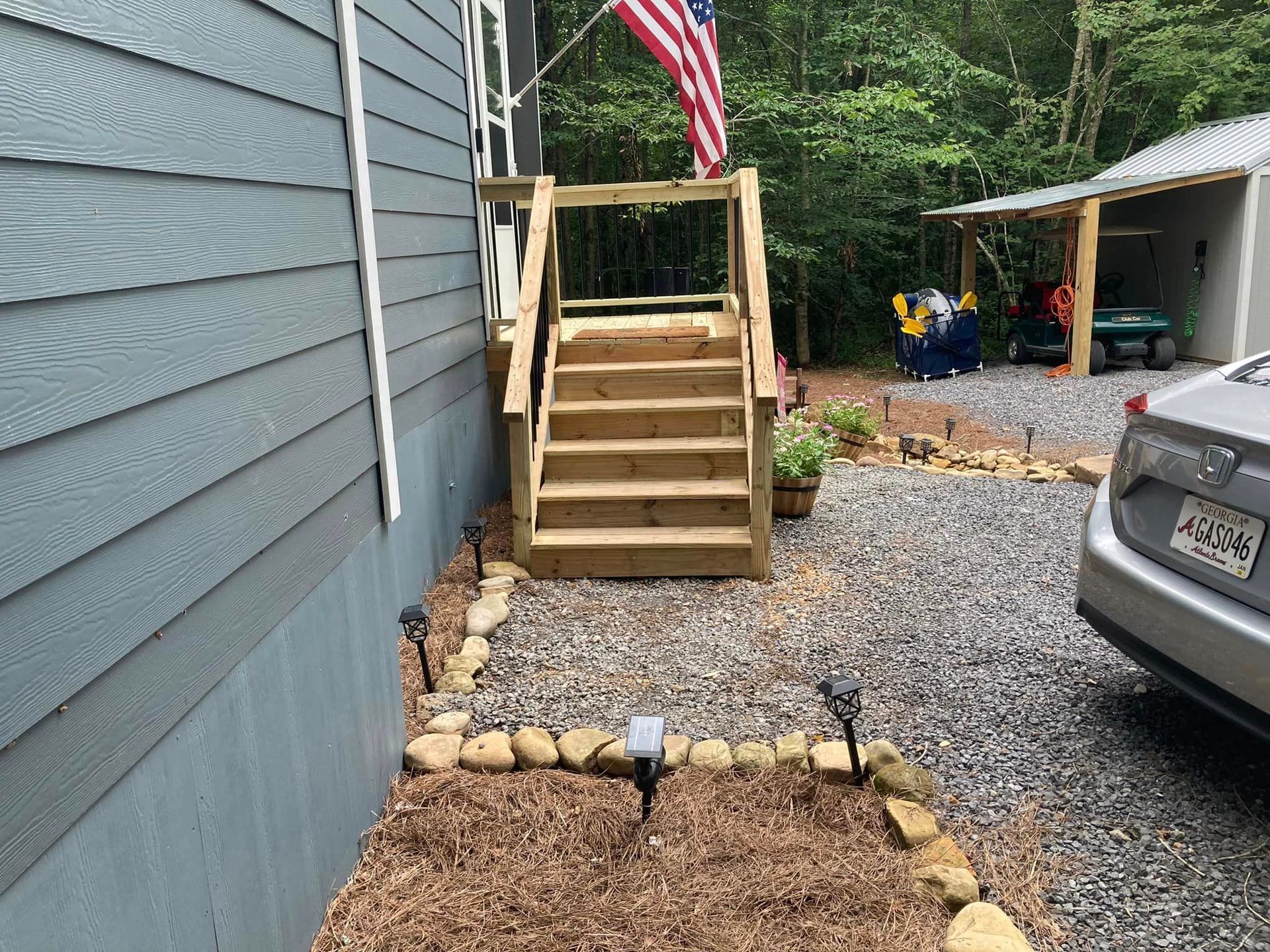 A car is parked in front of a house with stairs and an american flag.