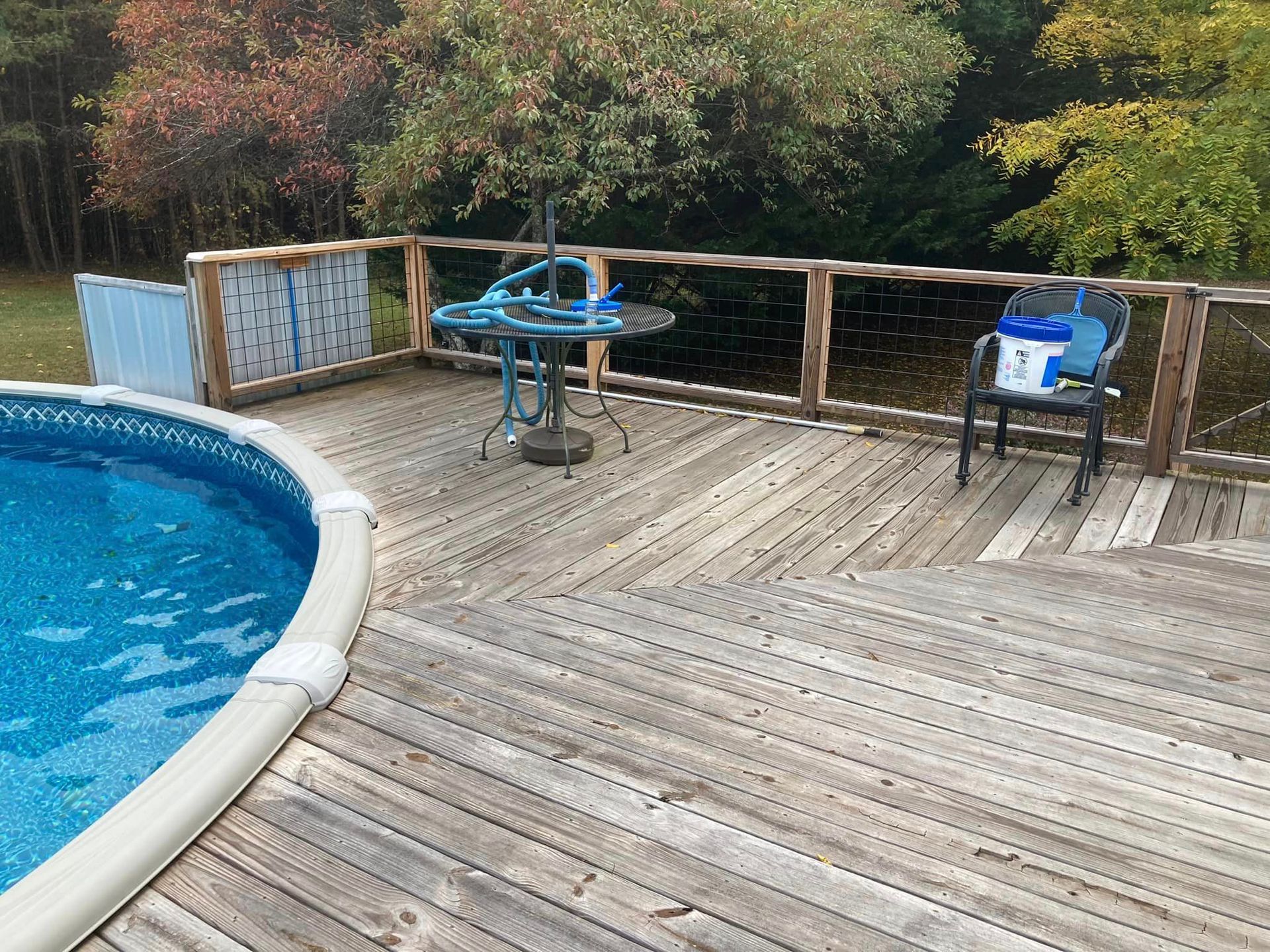 A wooden deck next to a swimming pool with a table and chairs.