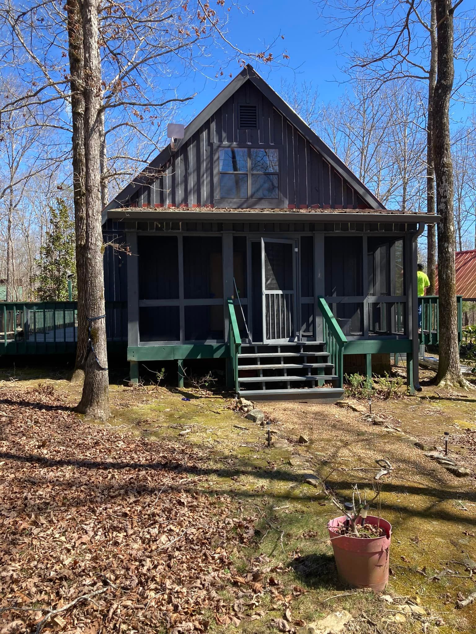 A small house with a screened in porch is surrounded by trees.