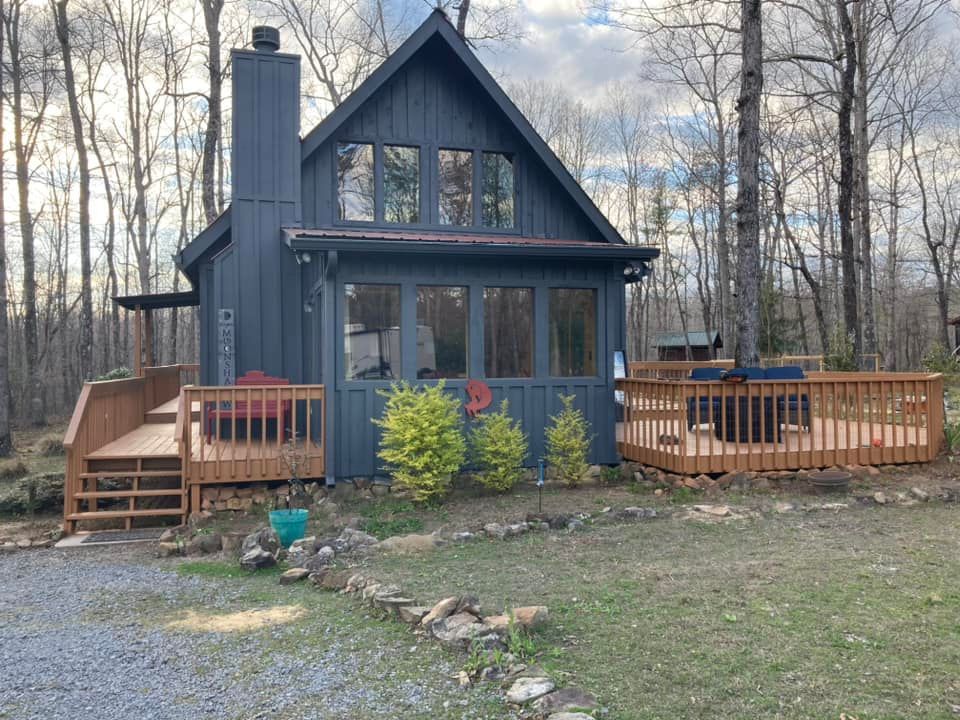 A small black house with a large deck in the woods.