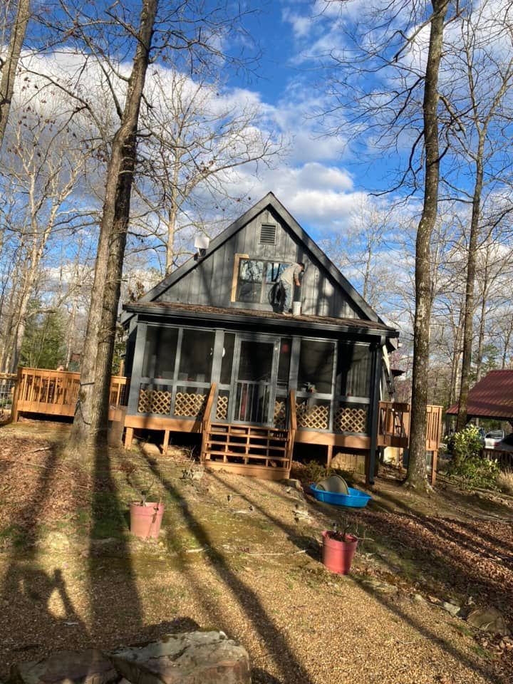 A small house with a screened in porch in the middle of a forest.