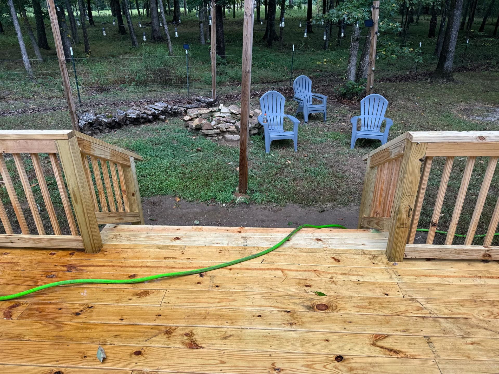 A wooden deck with blue chairs and a green hose.