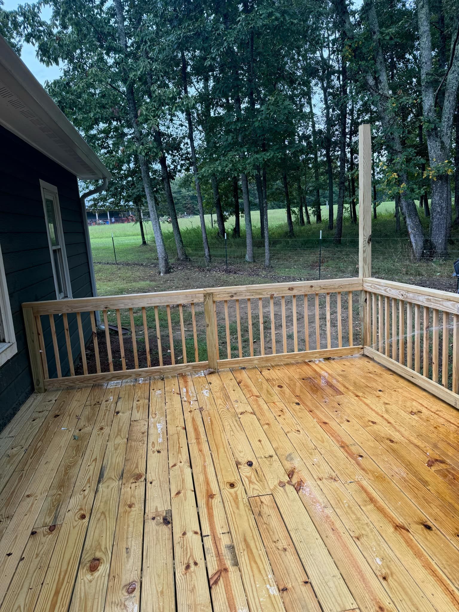 A wooden deck with a railing and trees in the background.