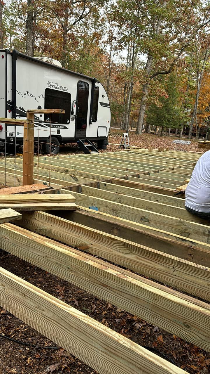 A man is sitting on a wooden deck next to a rv.