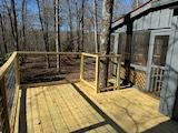 A wooden deck with a railing in front of a house in the woods.