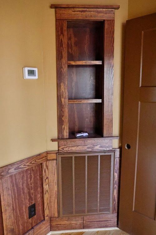 A wooden shelf with shelves and a door in a corner of a room.