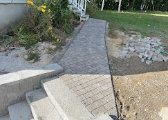 Stone-paved walkway beside steps, leading through a landscaped outdoor area with dirt and rocks.