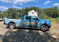 Blue Grimder? pickup truck parked on a gravel lot with trees and a house in the background