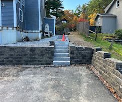 Outdoor concrete steps between retaining walls leading up to a driveway, marked by an orange cone.