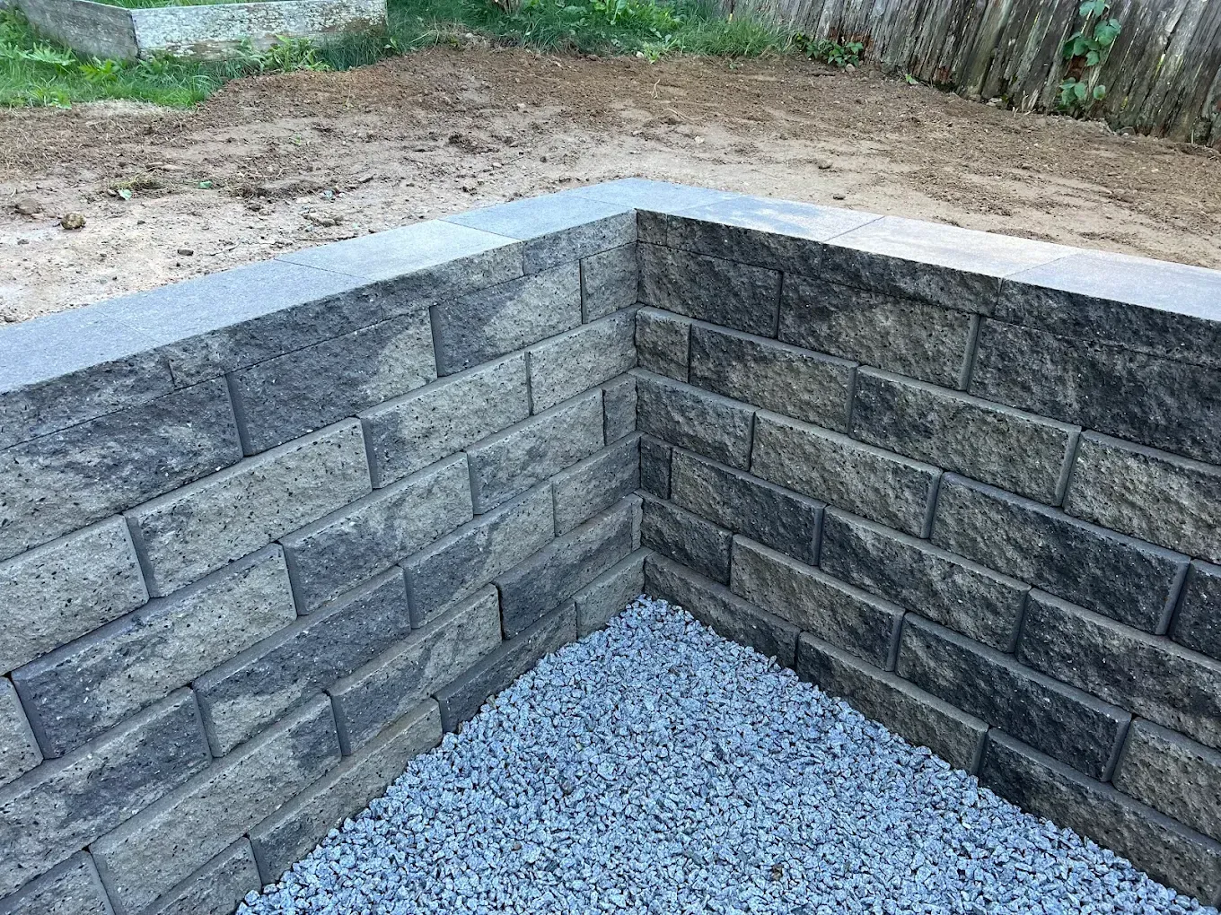Gray stone retaining wall corner with gravel base in an outdoor area
