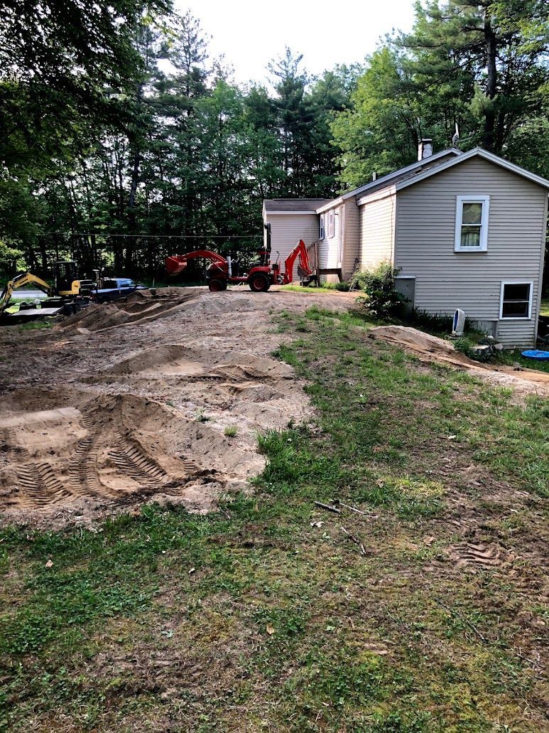 Backyard with a dirt excavation area beside a small gray house and trees