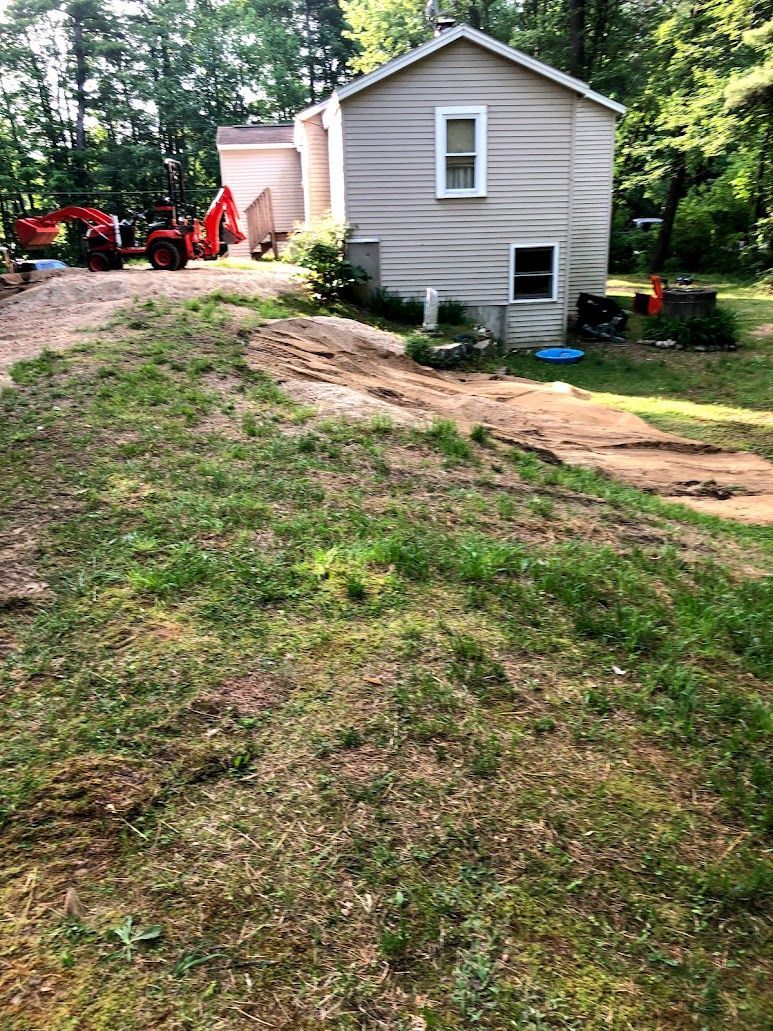 Grassy yard with a dirt path leading to a small gray house and red tractor in the background