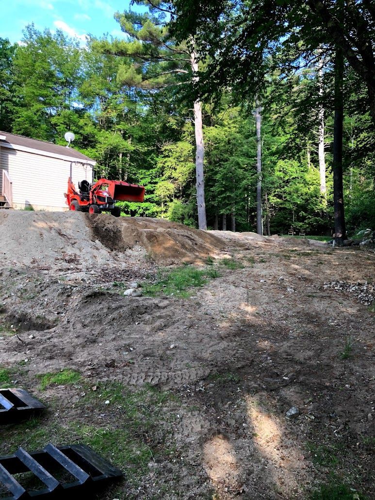 Red tractor on a dirt slope beside a white shed and wooded area