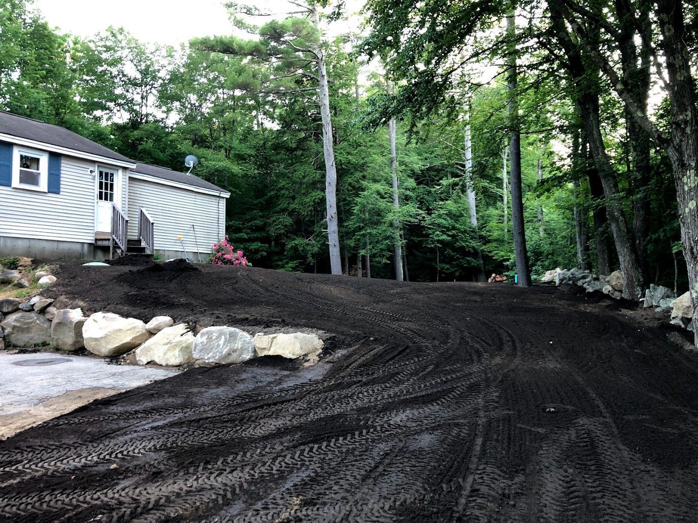 House beside freshly graded dirt driveway in wooded yard