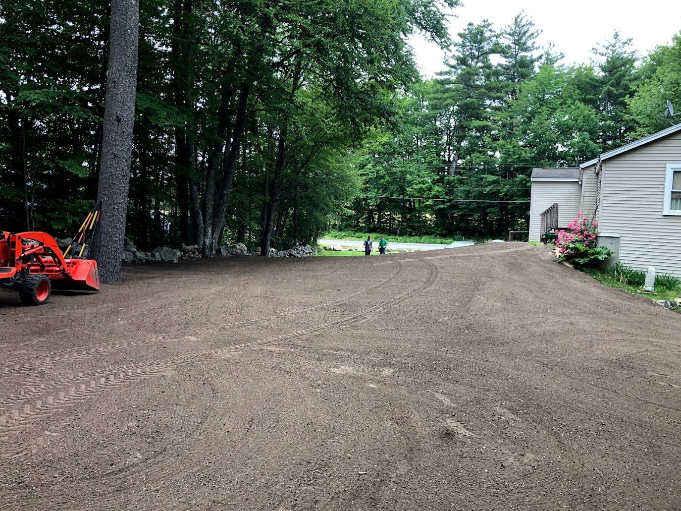 Gravel driveway beside a house, with trees and a small orange tractor on the left.