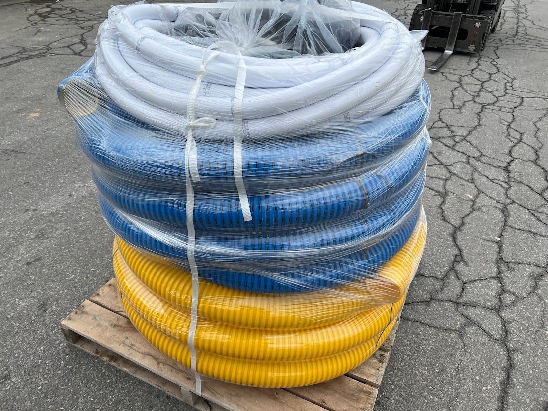 Stacked blue, yellow, and white coiled hoses wrapped on a pallet outdoors.