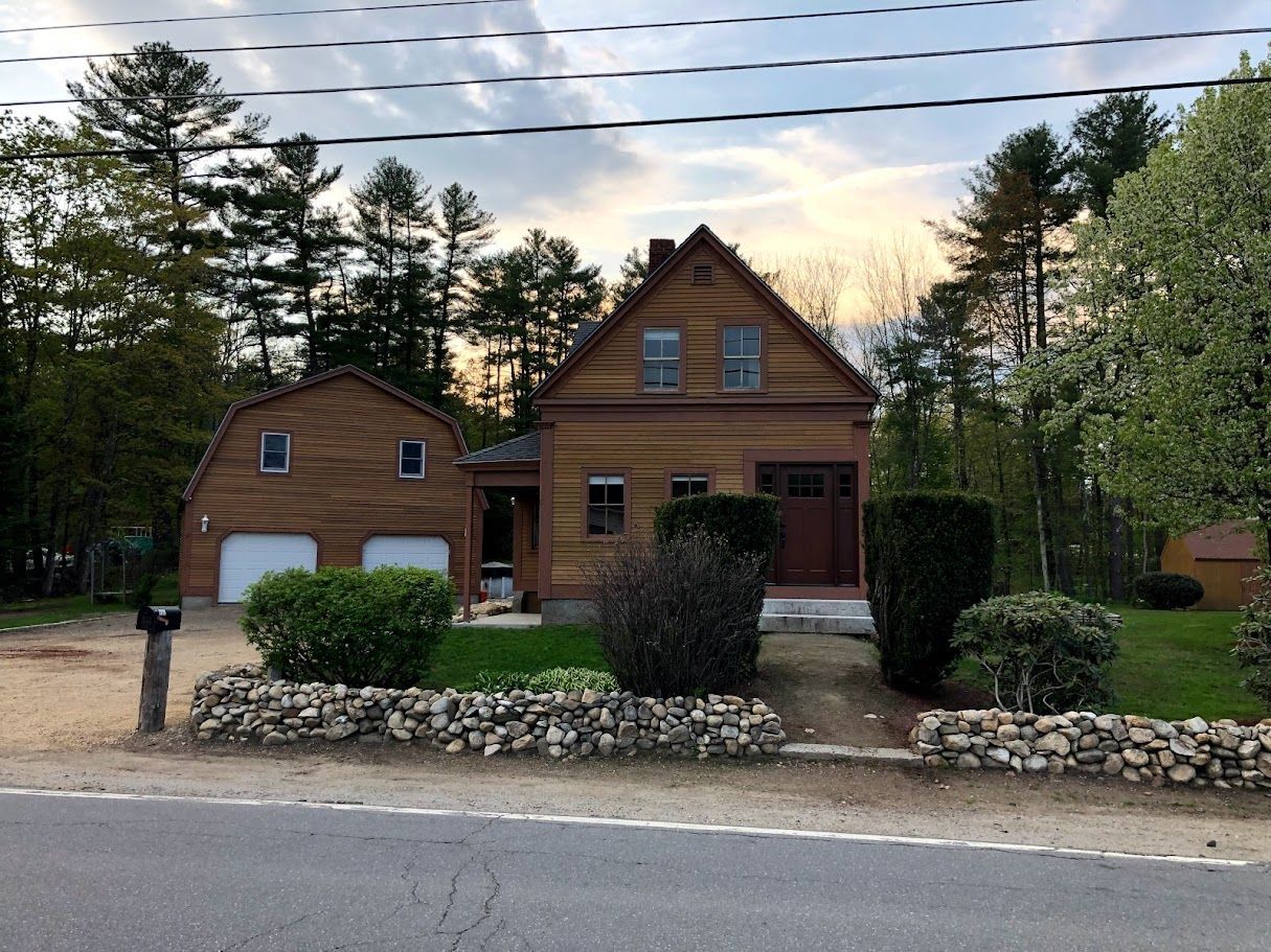 Wooden house with a garage and stone landscaping beside a road, framed by trees at dusk