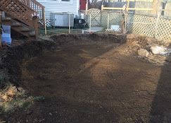 Backyard with freshly leveled dirt beside a house and wooden fence.