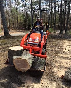 Person on orange tractor hauling a large cut log in a wooded area