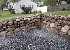 Stone retaining wall around a gravel yard in a residential backyard
