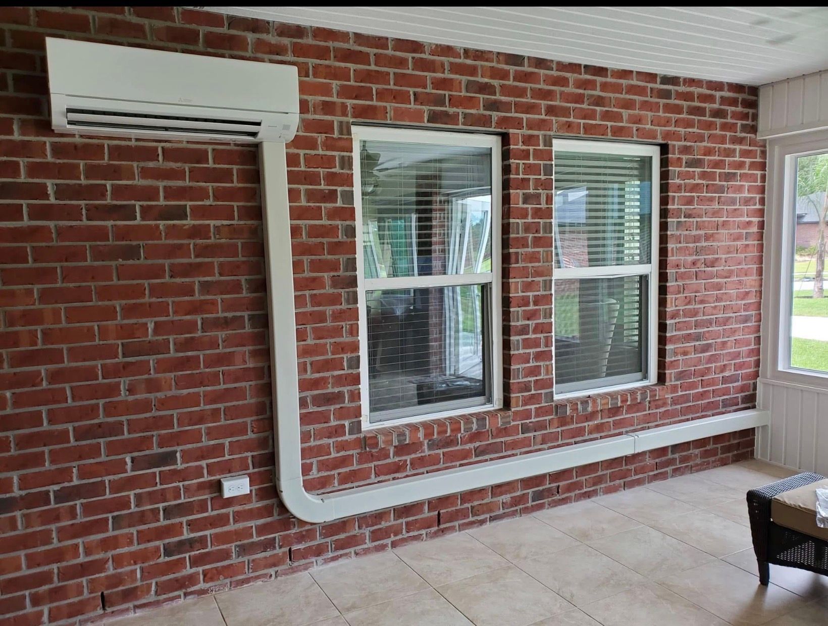 Brick patio with wall-mounted air conditioner and two windows beside a wicker chair