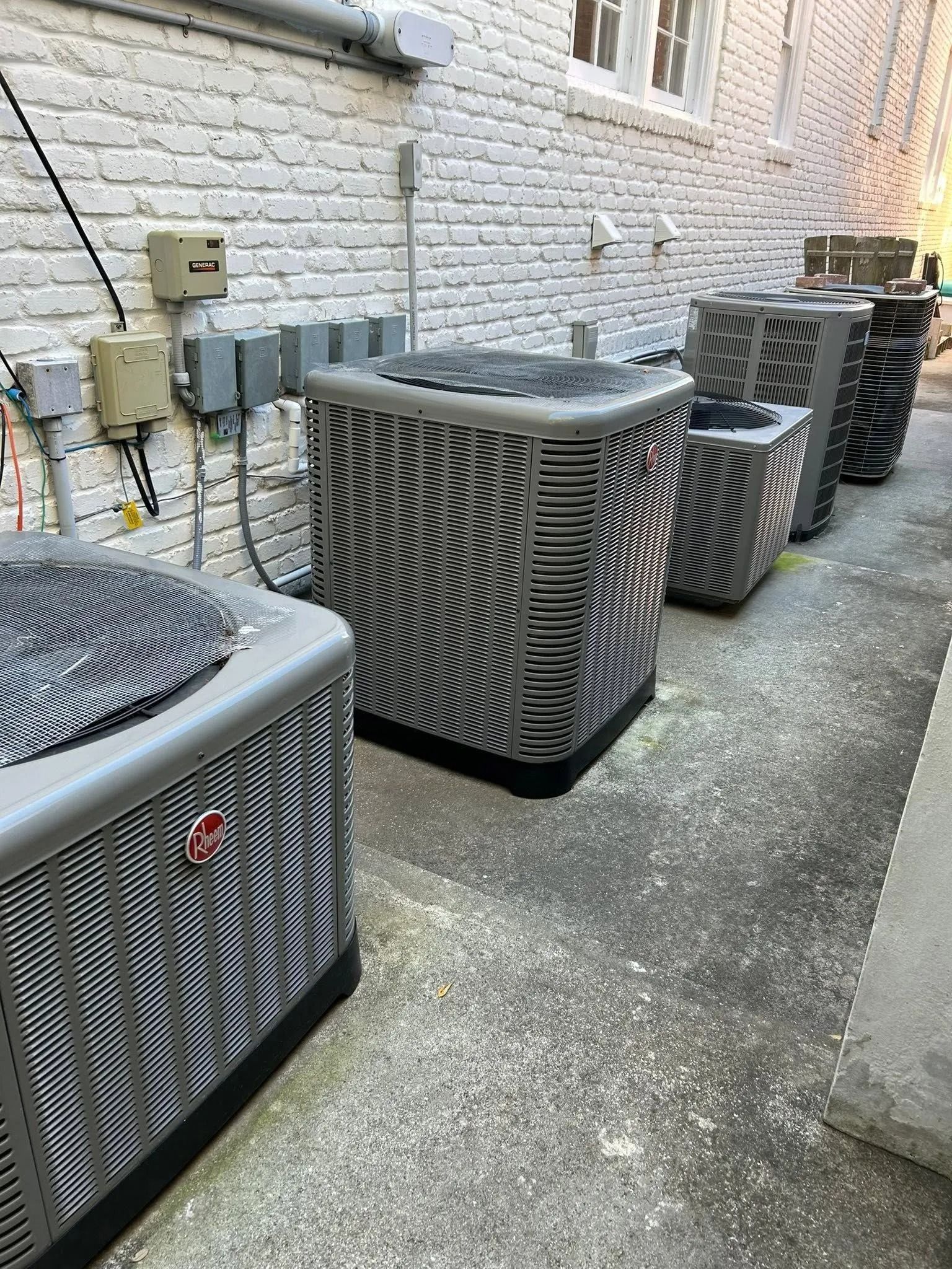 Row of outdoor HVAC units beside a white brick wall in an alleyway