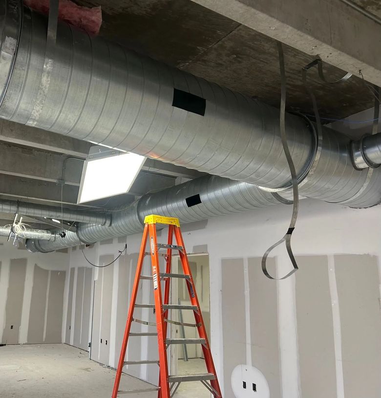 Orange ladder under silver ductwork in an unfinished room with drywall and exposed ceiling