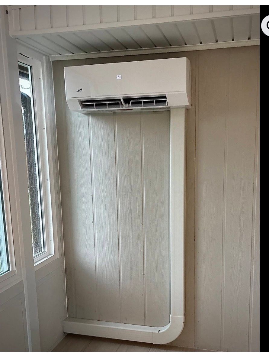 White wall-mounted air conditioner above a window in a small room