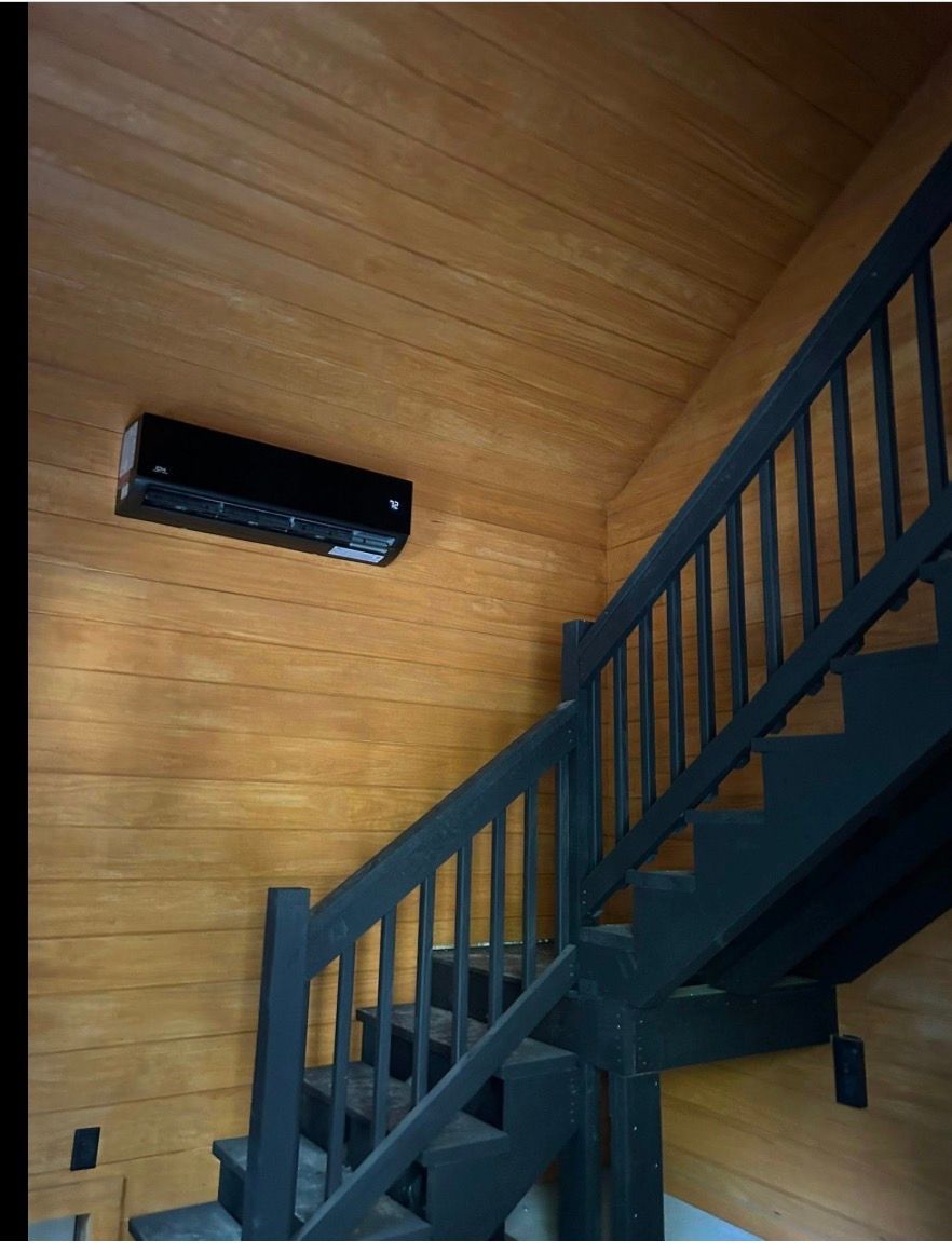 Wood-paneled room with a dark staircase and a wall-mounted black heater.
