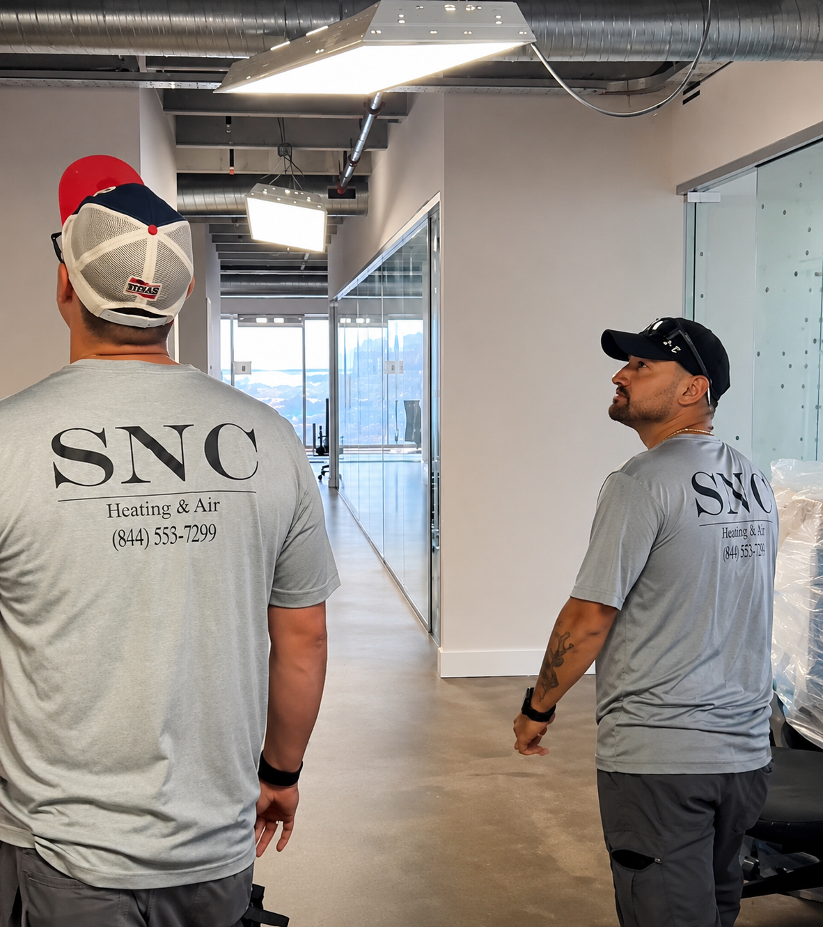 Two workers in gray SNC shirts walking through an office hallway under construction