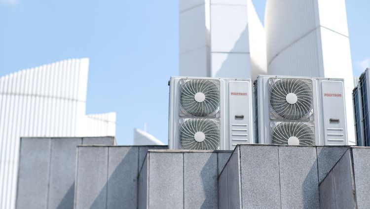 Two air-conditioning units on a rooftop beside a white modern building under a blue sky