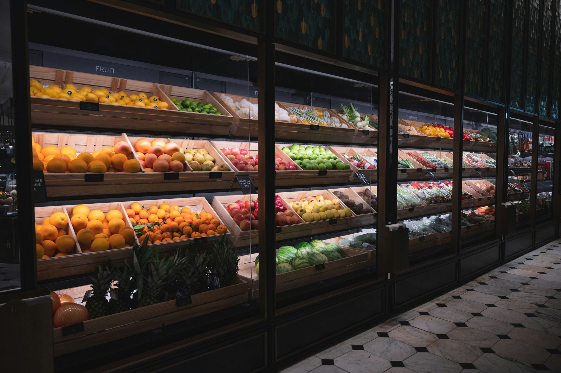 Bright produce display in a grocery store with rows of fruits and vegetables under glass cases