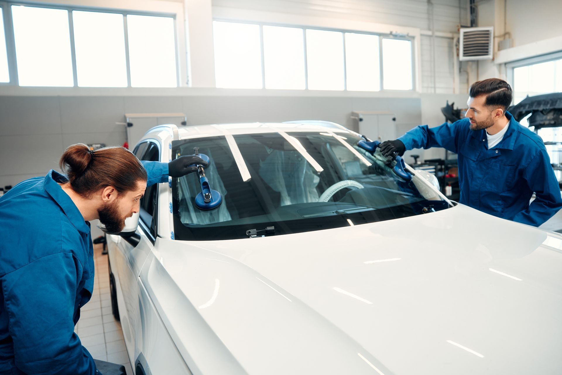Automobile workers are performing a car glass replacement in an auto service station garage. Automobile workers are performing a car glass replacement in an auto service station garage.