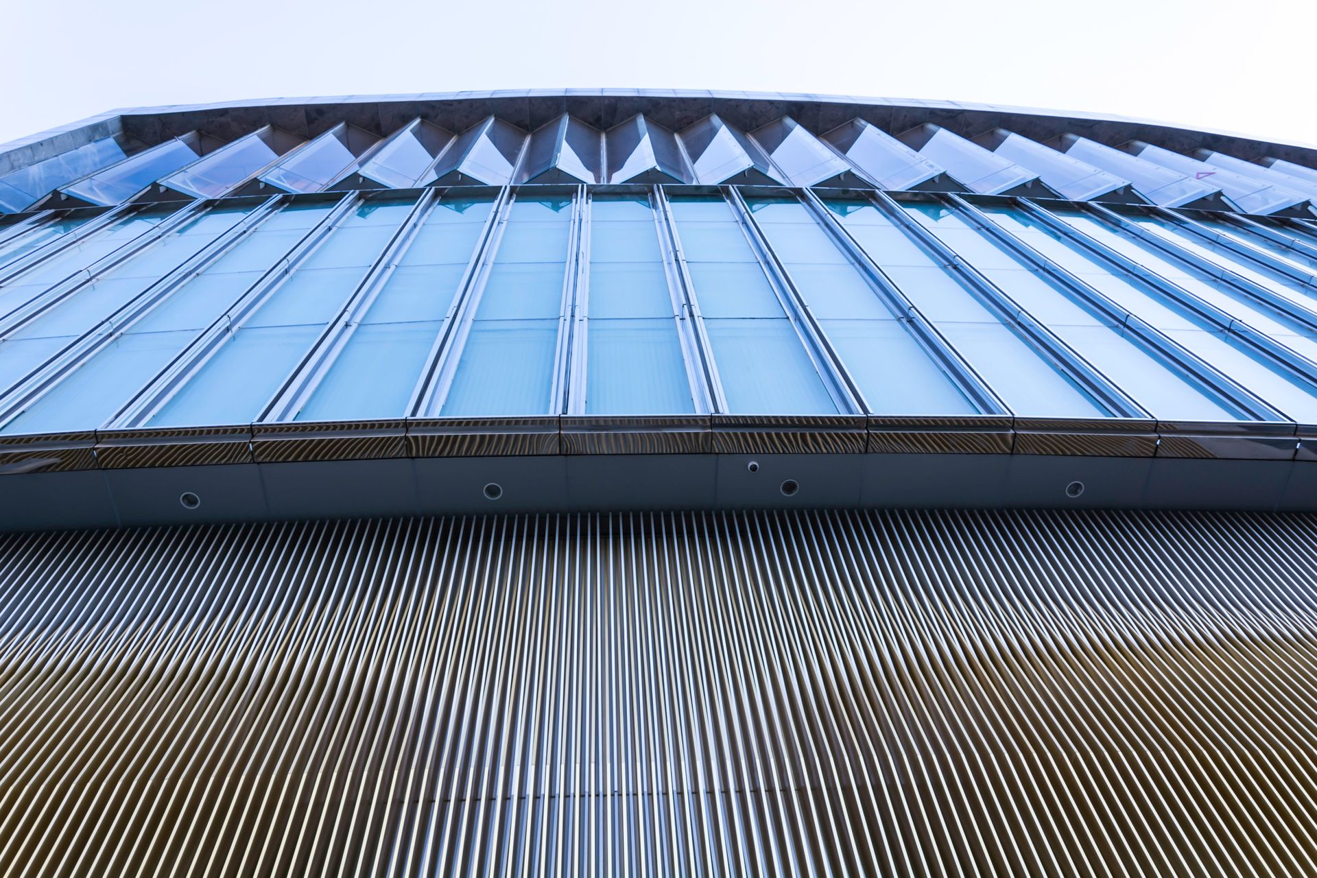 Vista en contrapicado de un edificio moderno con fachada de cristal y exterior estampado que refleja el cielo.