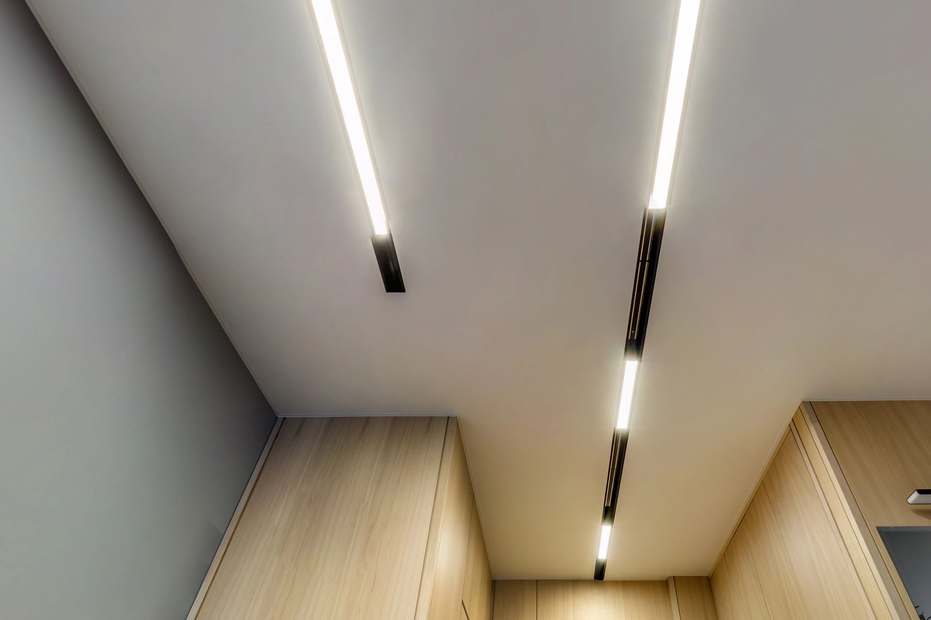 Luces LED lineales y brillantes instaladas en un techo blanco sobre paneles de madera clara.