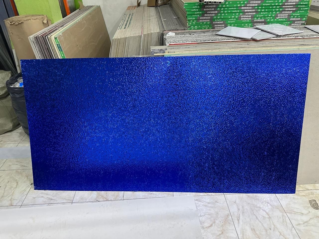 Superficie rectangular cubierta de purpurina azul, posiblemente un panel decorativo, en un entorno de taller desordenado.