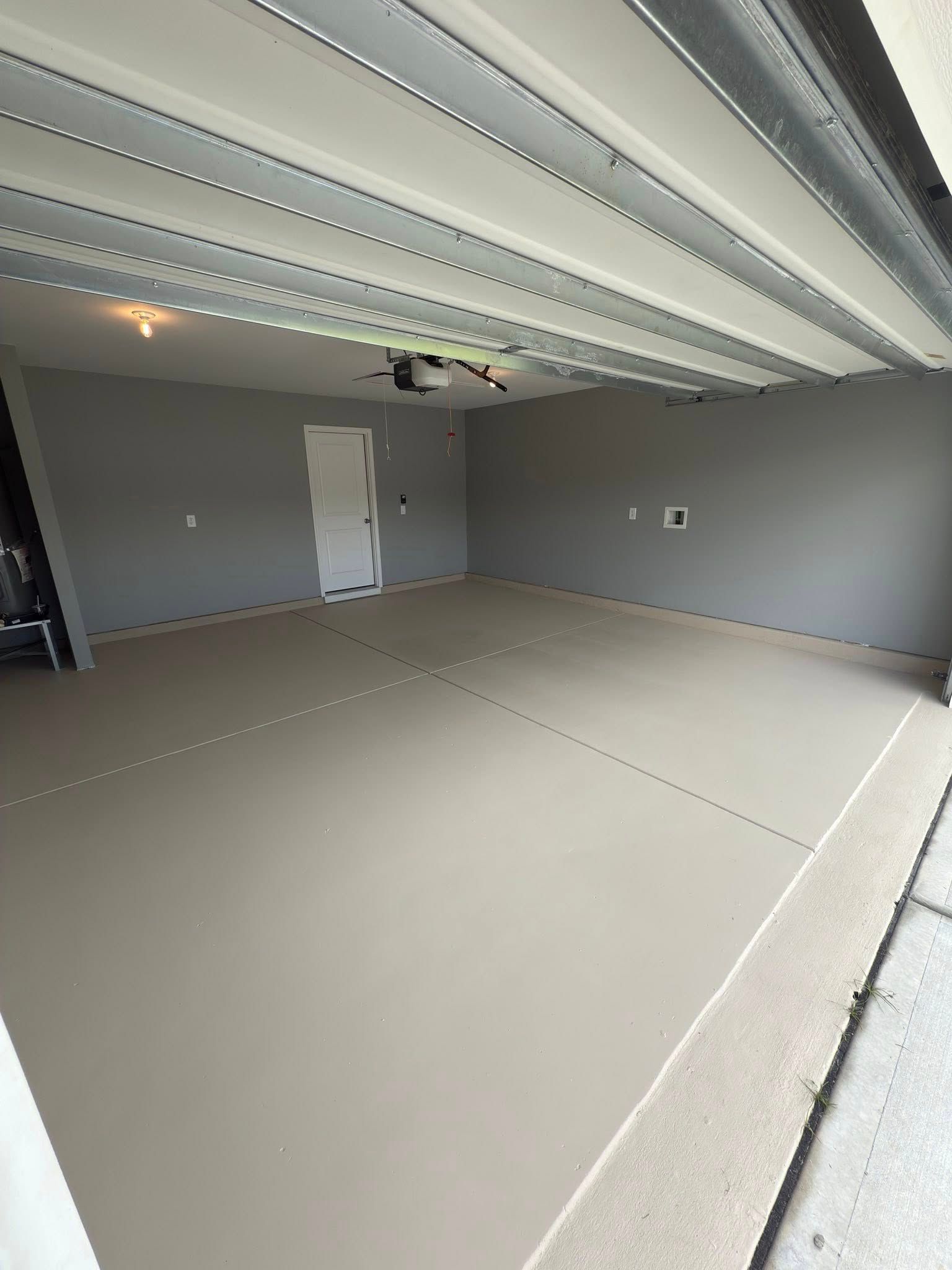 Empty, freshly painted garage with light tan floor and gray walls. Open garage door.