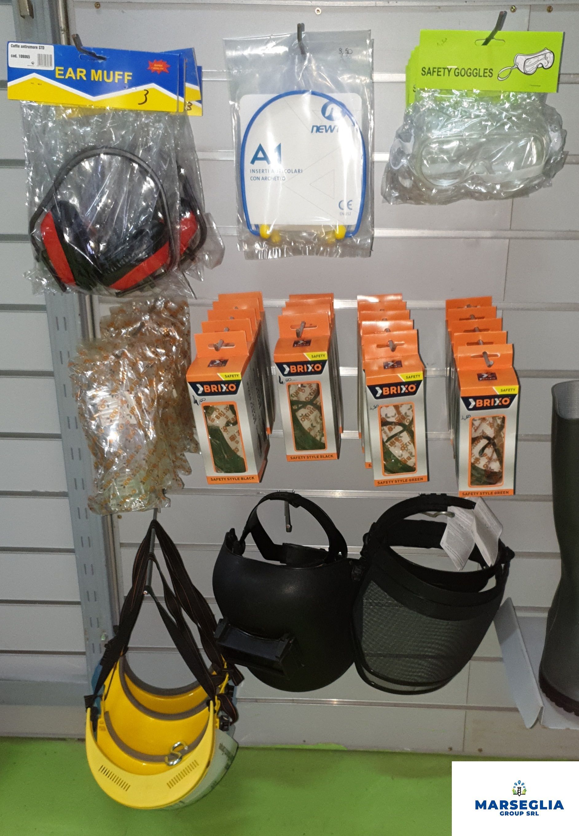 Esposizione di dispositivi di sicurezza su una parete del negozio, tra cui cuffie antirumore, respiratori, visiere protettive e una borsa per il trasporto.