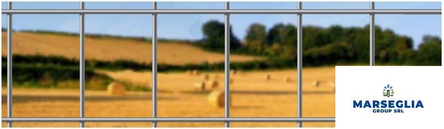 Vista di un campo attraverso una griglia metallica. Il campo è ricoperto di balle di fieno. Logo di Marsegia Group Srl.