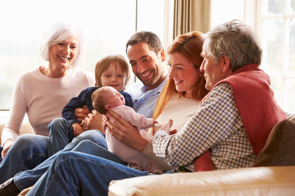 Family gathered on a couch, smiling and holding a newborn baby in a warm living room.